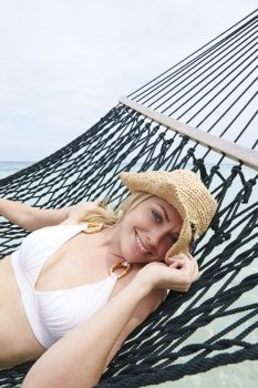 Woman Wearing Bikini And Sun Hat Relaxing In Beach Hammock