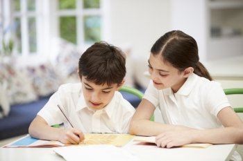 Children Wearing School Uniform Doing Homework In Kitchen