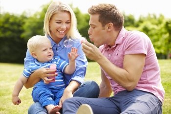 Parents Blowing Bubbles For Young Boy In Garden
