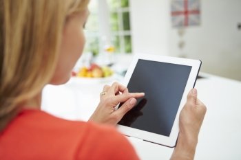 Woman Using Digital Tablet At Home In Kitchen
