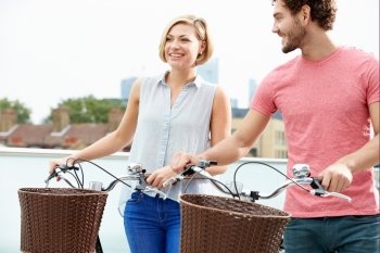 Couple Pushing Bikes With City Skyline In Background
