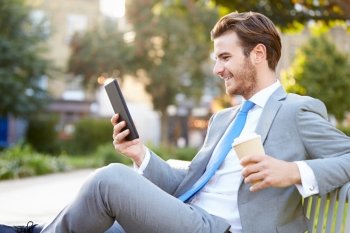 Businessman On Park Bench With Coffee Using Digital Tablet