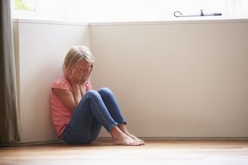 Unhappy Child Sitting On Floor In Corner At Home