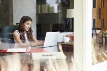 View Of Teenage Girl Using Laptop Through Window