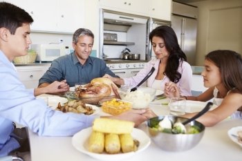 Family Sitting Around Table Saying Prayer Before Eating Meal