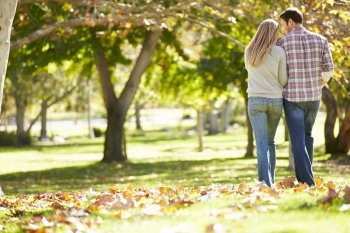 Rear View Of Romantic Couple Walking Through Autumn Woodland