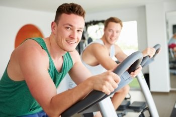 Two Young Men Training In Gym On Cycling Machines Together
