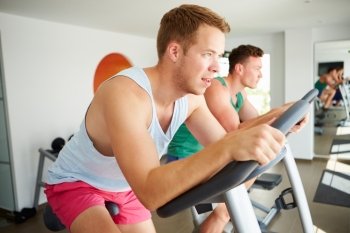 Two Young Men Training In Gym On Cycling Machines Together