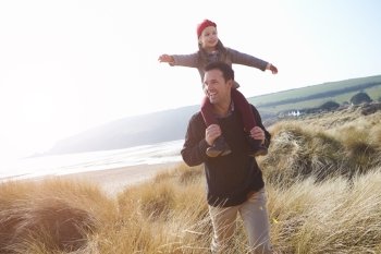 Father And Daughter Walking Through Dunes On Winter Beach