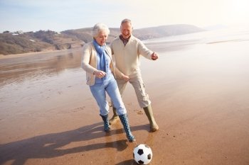 Senior Couple Playing Football On Winter Beach