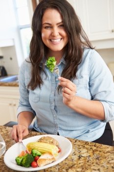 Overweight Woman Eating Healthy Meal In Kitchen