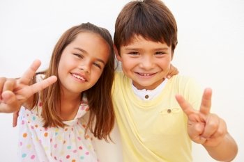 Hispanic Boy And Girl Standing By Wall Making Peace Sign