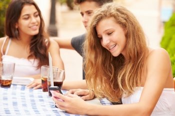 Teenage Girl Using Mobile Phone Sitting At Caf‚ With Friends