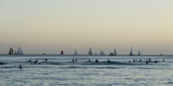 Surfers and sailboats in the ocean at sunset, Waikiki, Honolulu, Oahu, Hawaii, USA