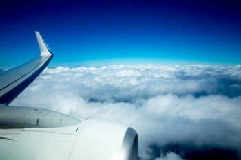 Airplane wing flying over fluffy clouds in blue sky high view