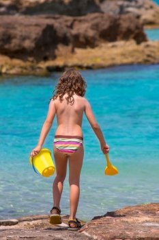 Kid girl rear view in beach tropical turquoise water with bucket and spade