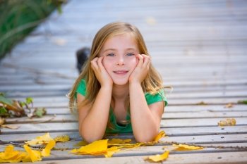 Kid girl in autumn wood deck with yellow leaves relaxed outdoor