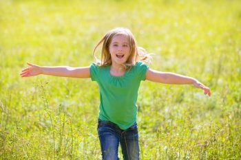 Blond kid girl happy running open hands smiling in outdoor green meadow