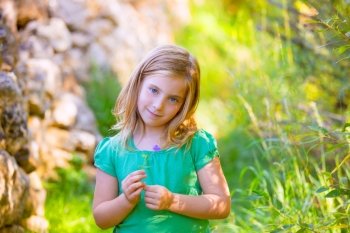 Blond kid girl smiling with purple flower relaxed in green outdoor