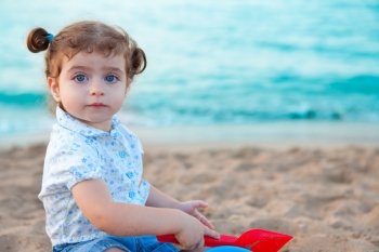 Blu eyes brunette toddler girl playing with sand in beach at mediterranean