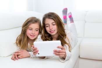 Children sister friends kid girls playing together with tablet pc lying on white sofa