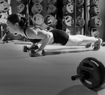 Push-ups woman with dumbbells workout fitness club at weightlifting gym