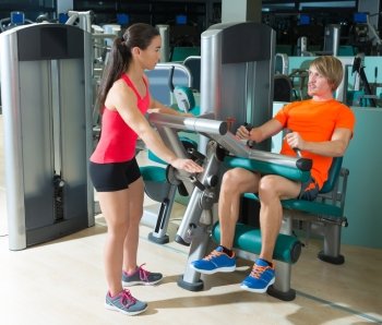 Gym seated leg curl machine exercise blond man and personal trainer woman