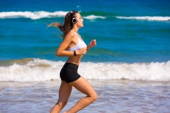 Brunette girl running on the beach with headphones