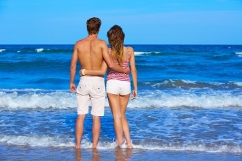 Young couple standing looking at the beach rear back view
