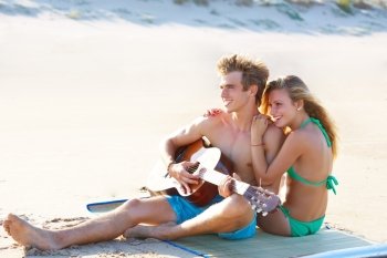 Blond couple sitting in the beach sand playing guitar in summer vacation