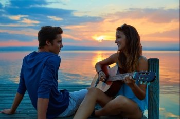 Couple playing guitar in sunset pier at dusk beach happy together