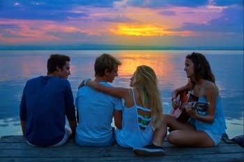 Friends group playing guitar in sunset pier at dusk beach happy
