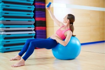 Pilates woman shoots selfie self portrait with mobile at gym relaxed with fitball