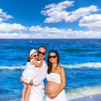 Happy family on the beach posing relaxed with pregnant mother woman