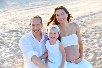 Family with pregnant mother on the beach sand happy in summer vacations