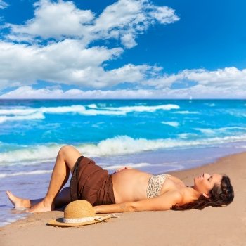 Beautiful pregnant woman on the beach lying on sand