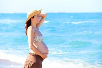 Beautiful pregnant woman on the beach with hat