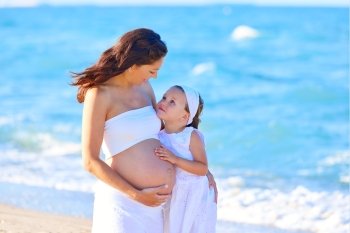 Pregnant mother and daughter on the beach together hug
