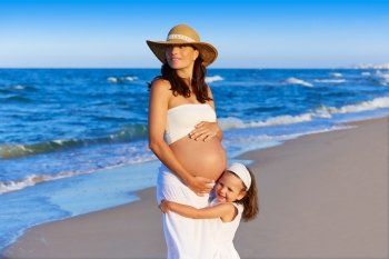 Pregnant mother and daughter on the beach together hug happy in summer