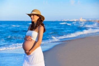 Beautiful pregnant woman on the beach with hat touching her belly