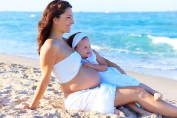 Pregnant mother and daughter on the beach together hug
