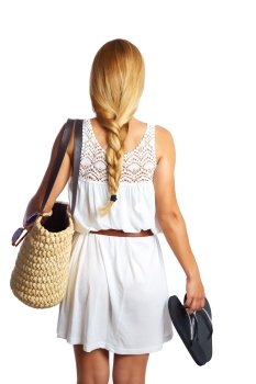 Blond tourist girl with flip flop shoes white summer dress and basket bag going beach rear view