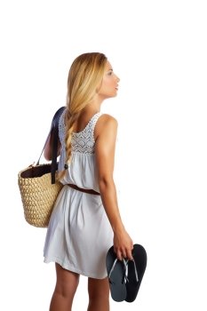 Blond tourist girl with flip flop shoes white summer dress and basket bag going beach rear view