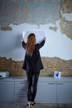 Architect woman holding plan on wall full length rear view at office