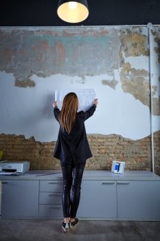 Architect woman holding plan on wall full length rear view at office