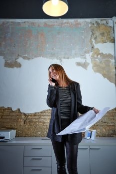 Architect woman talking phone holding plan paper at office