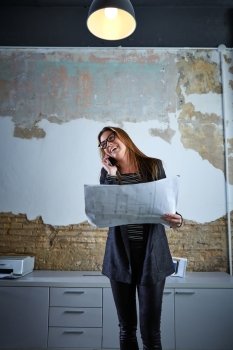 Architect woman talking phone holding plan paper at office