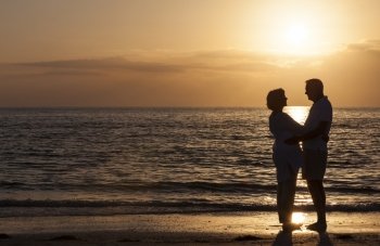 Happy senior man and woman couple together hugging embracing at sunset on a deserted tropical beach 