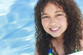 A cute happy young interracial African American girl child relaxing on the side of a swimming pool smiling