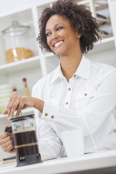 A beautiful happy mixed race African American girl or young woman making coffee with a cafetiere in her kitchen at home
